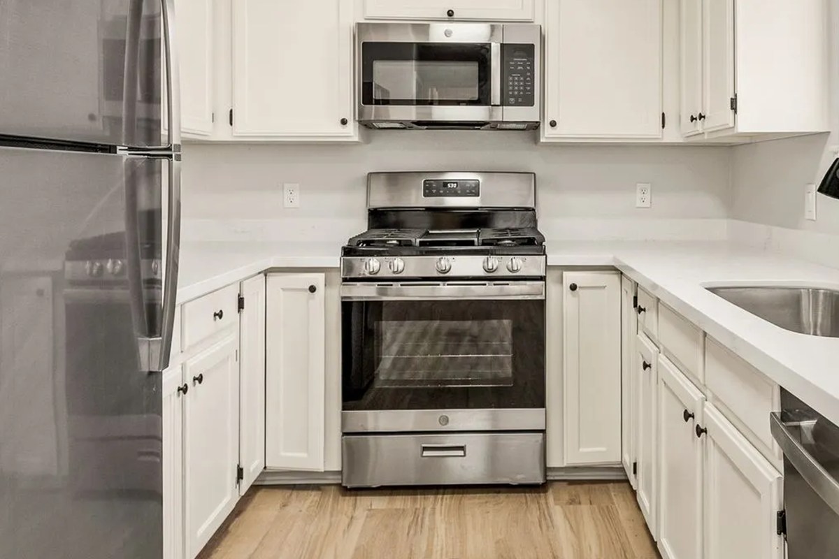 The same Venture on Lockett kitchen after renovation: white shaker cabinets, stainless appliances, quartz counters and wood-look plank flooring