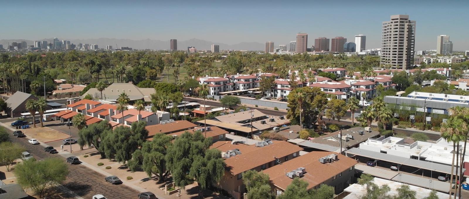Aerial view of multifamily apartment properties, palm trees, and a downtown skyline on the horizon